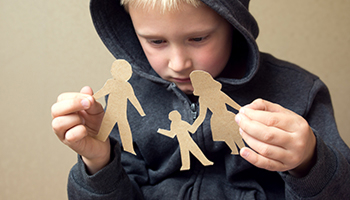 A child in a dark grey hoodie holds up two paper cutouts, one of a mother and one of a father.