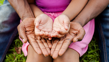 A child's small hands rest inside the larger hands of an adult.