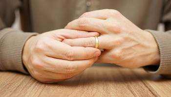 A close-up of a man's hands on a wooden table as he prepares to remove his wedding ring.