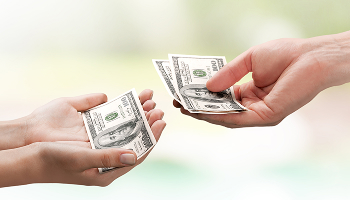 One person's hand with several $100 bills is being given to another person's hand.